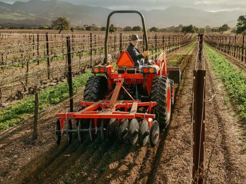 Extensive Field Maintenance with Riding Mower Outdoor maintenance worker riding a mower across a large field.